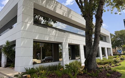Corner of the white two-story building with its ribbon windows, mature trees and landscaping