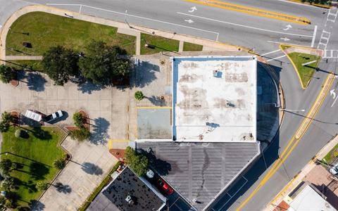 Straight-down aerial of the roof, the paver forecourt and the parking area behind the building